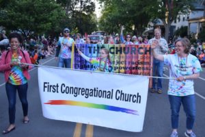 Numerous church members marching during the Ithaca Festival Parade, holding banners that say "First Congregational Church" with a rainbow and "Be the Church"