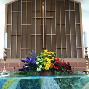 A rainbow bouquet of flowers on the altar in front of the cross
