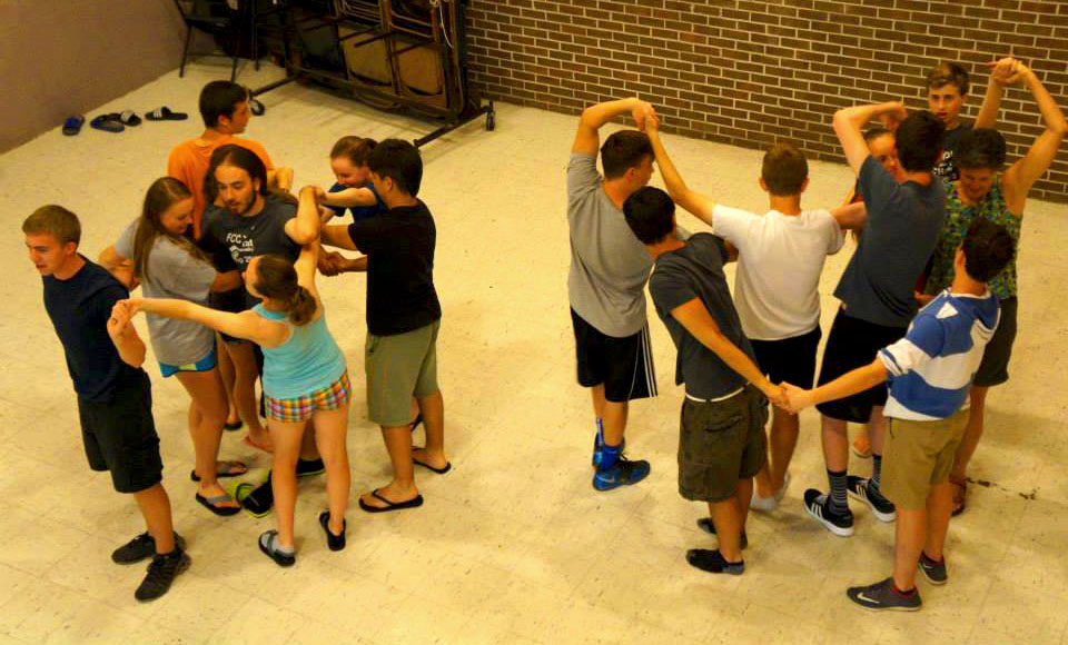 Two groups of 8 youth with their arms intertwined in a game or teambuilding exercise