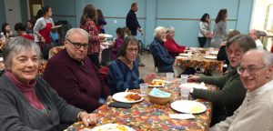 Several individuals around a table enjoying a churchwide meal in the fellowship hall