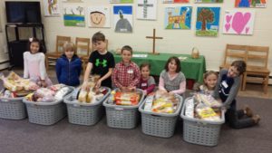 Eight youth sitting behind laundry baskets filled with food donated for Thanksgiving baskets