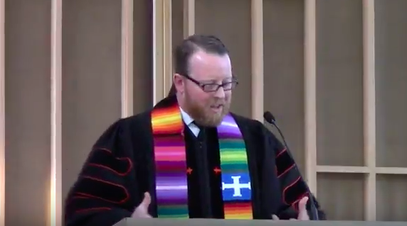 Senior Minister David Kaden wearing a multi-colored stole giving a sermon from the pulpit