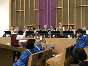 The choir, in blue robes, listening to the handbell choir perform a piece conducted by Bill Cowdery