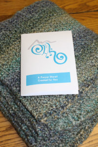 a gray prayer shawl folded with a card reading "A Prayer Shawl Created for You"