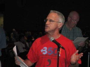 Jim Antal in red shirt speaking in front of a microphone